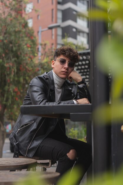 Attrayant homme latino aux cheveux bouclés et lunettes de soleil assis à l'extérieur