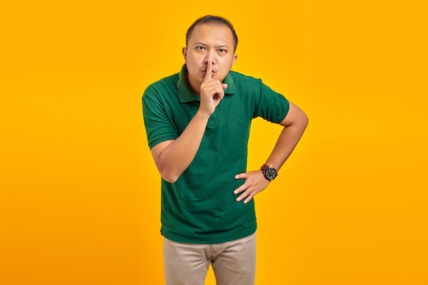 Attrayant jeune homme asiatique doigt sur les lèvres et faisant un geste silencieux sur fond jaune
