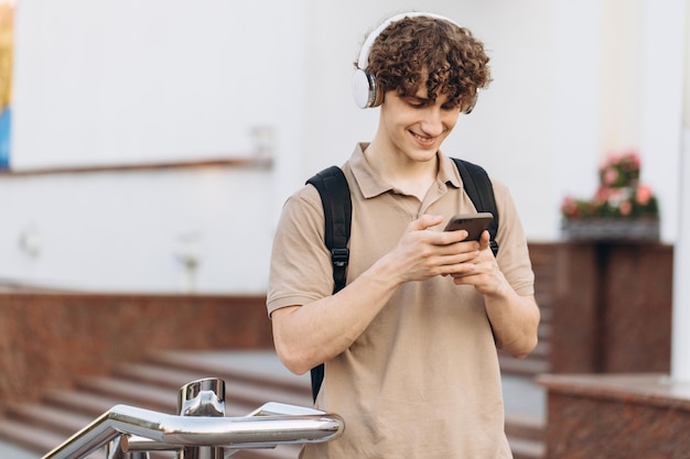 Attrayant jeune homme bouclé universitaire ou étudiant avec téléphone se promenant sur le campus