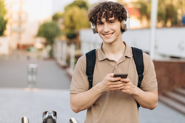 Attrayant jeune homme bouclé universitaire ou étudiant avec téléphone se promenant sur le campus