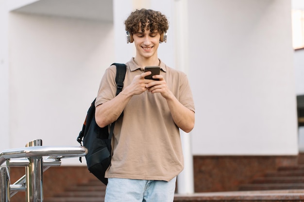 Photo attrayant jeune homme bouclé universitaire ou étudiant avec téléphone se promenant sur le campus