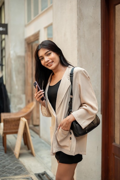 Une attrayante femme asiatique heureuse dans des vêtements à la mode se tient dans une rue commerçante de la ville