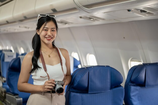 Une attrayante passagère asiatique se tient dans l'allée d'un avion en souriant à la caméra