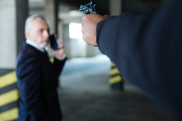 Photo au bout du fusil. mise au point sélective d'une arme de poing dirigée vers l'homme d'affaires tout en étant entre les mains d'un dangereux criminel endurci