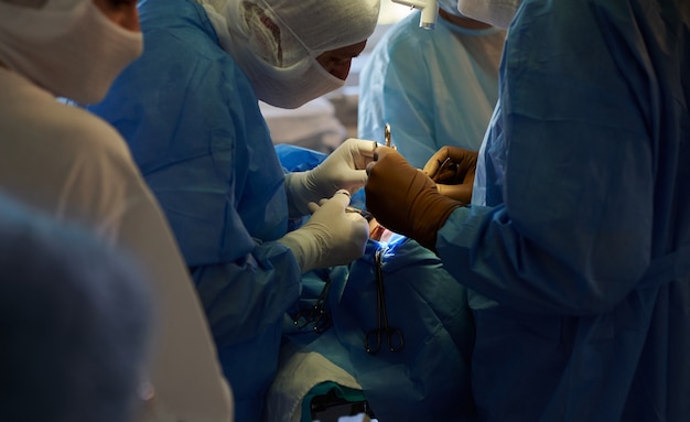 Au centre, deux chirurgiens effectuent une opération, derrière eux se trouve une infirmière opératrice