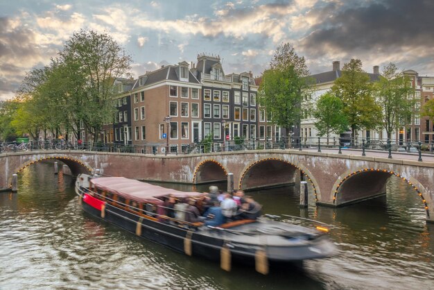 Au coucher du soleil d'été aux Pays-Bas sur les canaux d'Amsterdam, des bateaux de plaisance flottent entre les ponts, des maisons traditionnelles et des vélos sur le front de mer.