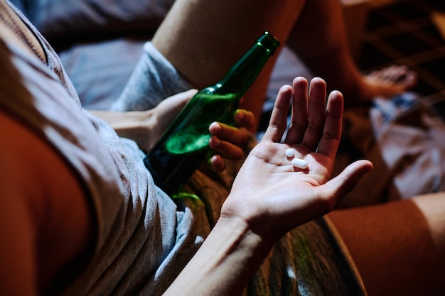 Photo au-dessus de l'angle de la main d'un jeune homme déprimé tenant des somnifères et une bouteille