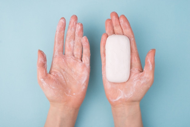 Au-dessus du haut, vue rapprochée, photo de mains utilisant une barre de savon et du savon crémeux isolés sur une surface de couleur bleue