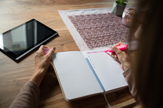 Au-dessus de l'épaule d'une femme écrivant une liste de choses à faire dans son bloc-notes sur une table en bois