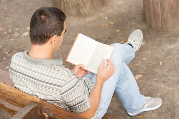 Au-dessus de l'épaule d'un homme en vêtements décontractés assis sur un banc en lisant un livre à la recherche sur les pages ouvertes