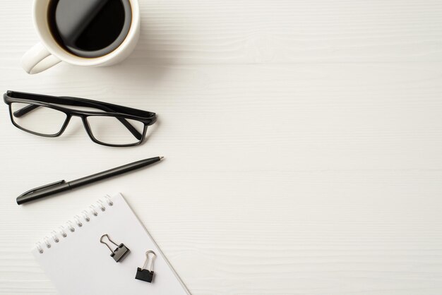 Au-dessus de flatlay voir photo de tasse de thé lunettes cahier spirale reliure stylo trombones et tasse de thé toile de fond en bois blanc isolé