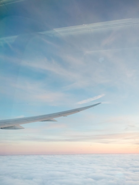 Au-dessus des nuages depuis la fenêtre de l'avion sous la lumière naturelle du crépuscule avec aile