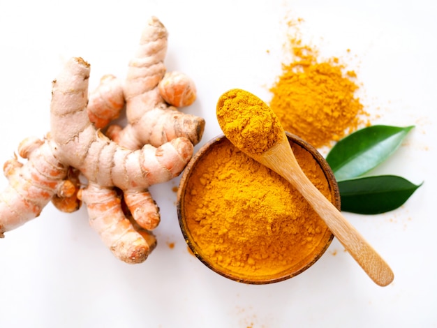 Au-dessus de poudre de curcuma dans un bol en bois et racine de curcuma, légumes à base d'herbes pour la peau ou la cuisson isolé sur une surface blanche.