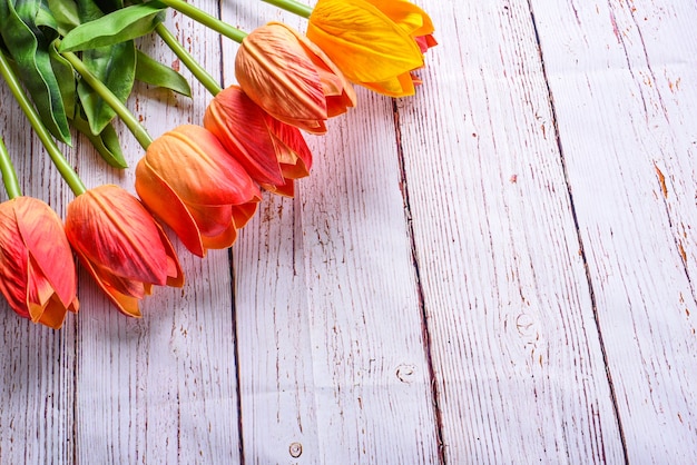 Au-dessus d'une table en bois rustique, un bouquet de tulipes orange et jaunes a été tiré au-dessus de la tête. Style de vue aérienne à plat.