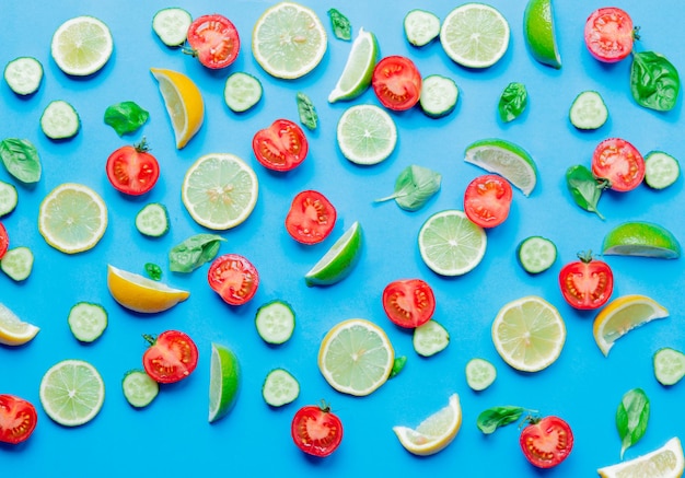 Au-dessus de la vue sur les citrons et les limes coupés et les tomates avec des concombres sur fond bleu