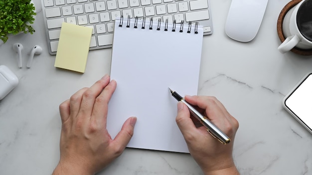 Au-dessus de la vue homme tenant un stylo et écrivant sur un cahier vide