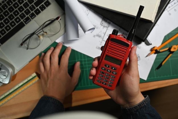 Au-dessus de la vue de la main de l'homme architecte tenant un talkie-walkie travaillant sur un plan au bureau en bois