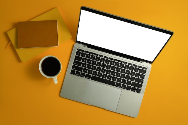 Au-dessus de la vue d'un ordinateur portable avec un bloc-notes vierge et une tasse de café sur fond jaune