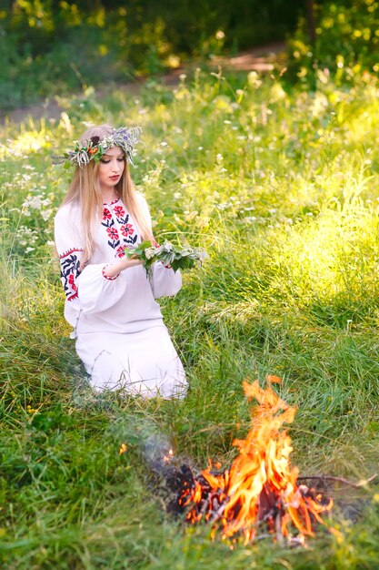 Au milieu de l'été. Femme tissant une couronne près du feu.