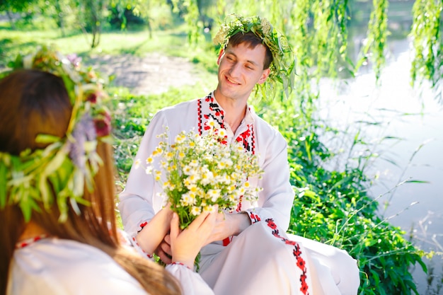 Au milieu de l'été. Jeune couple d'amoureux en costumes slaves sur la rive du lac. Fête slave d'Ivan Kupala.