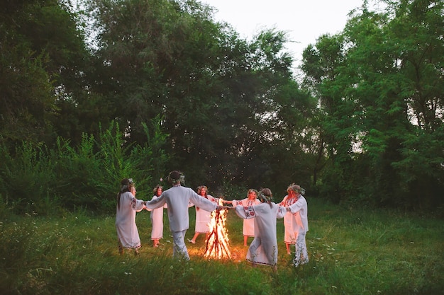 Au milieu de l'été. Des jeunes en vêtements slaves dansent en cercle autour d'un feu de joie dans la forêt.