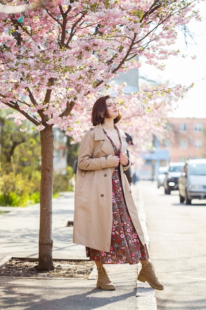 Au printemps, une femme marche le long d'une rue fleurie avec des arbres de sakura. Une fille dans une longue robe vintage élégante en soie marche parmi les arbres fleuris