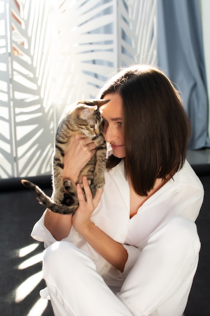 Photo au soleil, une jeune femme en chemise blanche tient un chaton gris dans ses bras