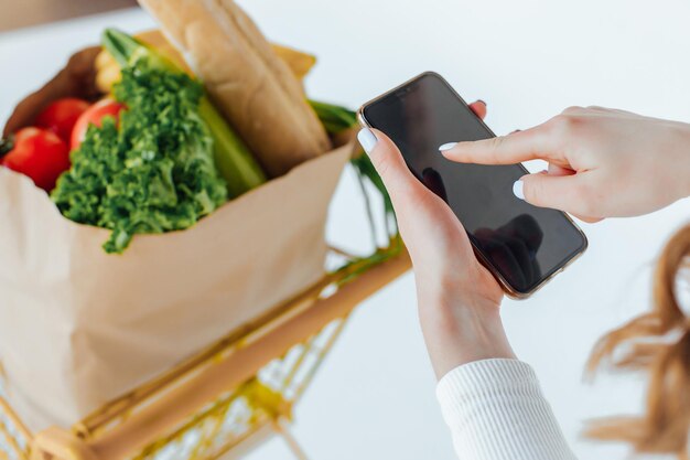 Au supermarché, la femme utilise un smartphone, s'appuie sur le panier.