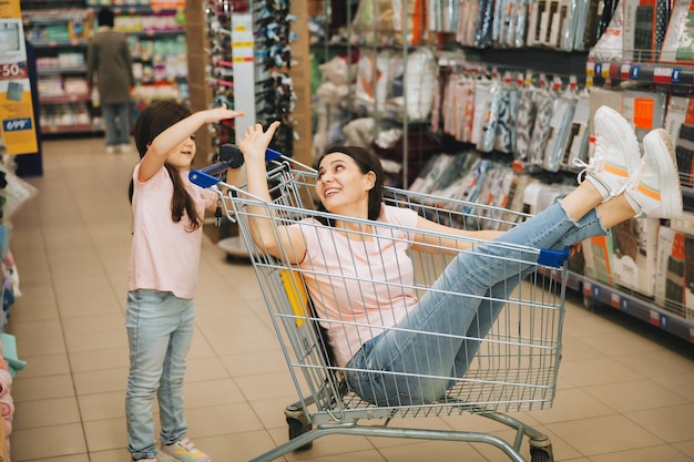 Au supermarché, une fille pousse un chariot avec une femme assise dedans une famille heureuse se précipite joyeusement sur le chariot du magasin