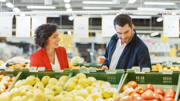 Au supermarché, un jeune couple heureux choisit des fruits biologiques dans la section des produits frais du magasin.