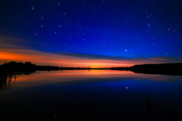L'aube du matin sur un fond de ciel étoilé se reflète dans l'eau du lac.