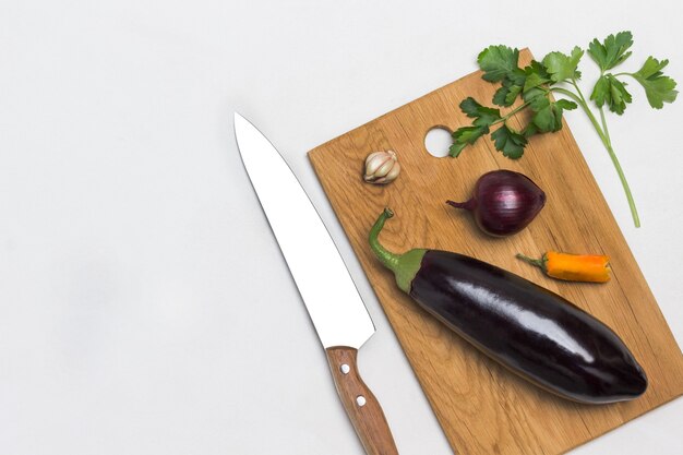 Aubergine et oignon sur planche à découper Brin de persil et couteau de cuisine sur table