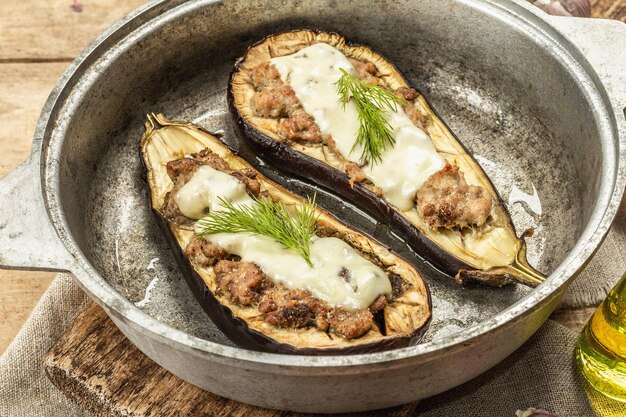 Aubergines farcies prêtes à manger avec de la viande hachée, des légumes et des épices. Fond en bois, ustensile de cuisine, style rustique, gros plan