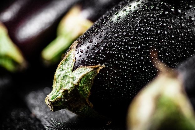 Des aubergines fraîches et mûres avec des gouttes d'eau sur une planche de pierre