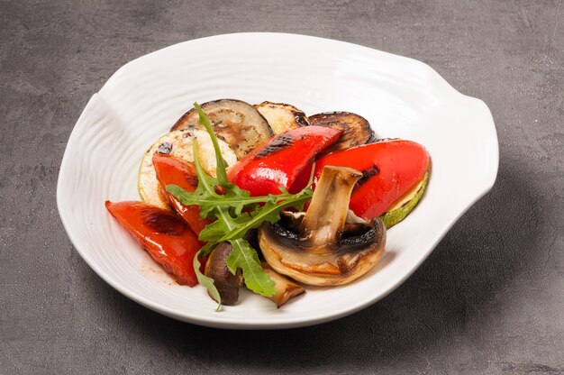 Aubergines savoureuses, courgettes, poivrons et champignons grillés sur une plaque blanche