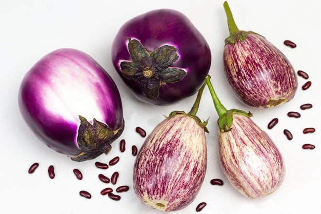 Aubergines violettes et rayées sur table. Graines de haricot. Mise à plat. Fond blanc.