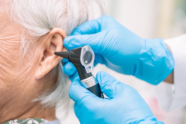 L'audiologiste ou le médecin ORL utilise un otoscope vérifiant l'oreille d'une patiente asiatique âgée traitant un problème de perte auditive.