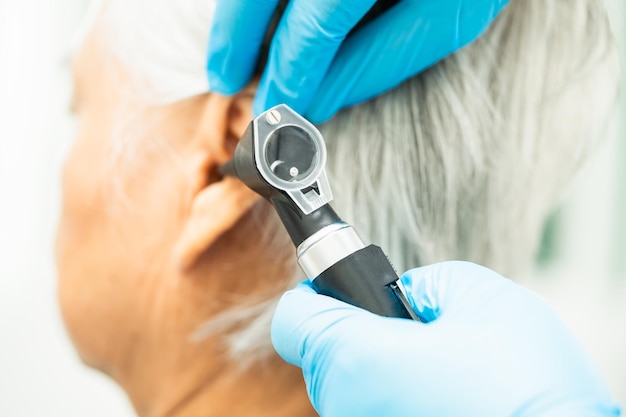 Audiologiste ou orthodontiste utilise un otoscope pour vérifier l'oreille d'une femme âgée asiatique traitant un problème de perte auditive