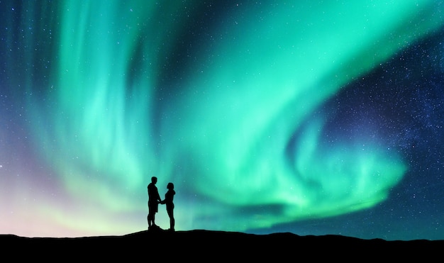 Aurores boréales et étreindre couple sur la colline. Paysage avec ciel étoilé de nuit, aurores boréales, silhouette d'homme et femme. Gens.