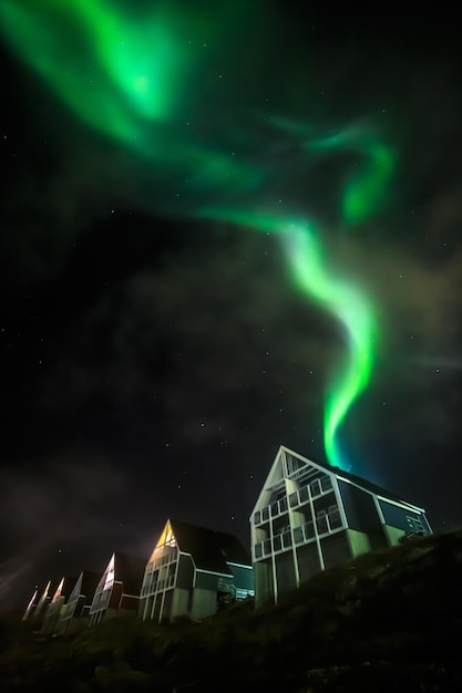 Aurores boréales lumineuses vertes partiellement cachées par les nuages au-dessus des maisons d'habitation des Inuits de la ville de Nuuk au Groenland