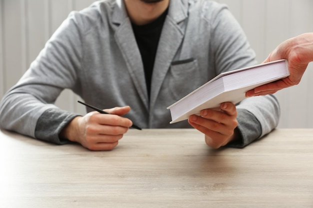 Auteur signant un autographe dans son propre livre à une table en bois sur fond de planches blanches