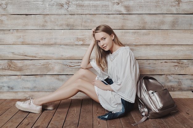 Authentique jeune fille blonde avec sac à dos argenté sur mur en bois