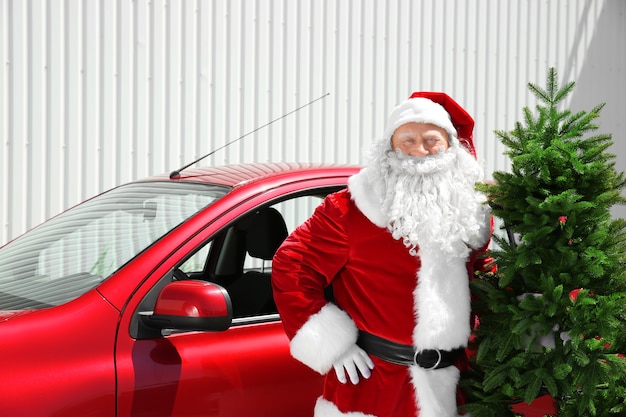 Authentique Père Noël avec arbre de Noël debout près de la voiture rouge à l'extérieur