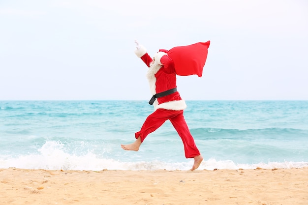 Authentique Père Noël avec grand sac rouge plein de cadeaux sur la plage