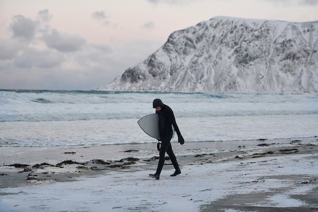 Authentique surfeur arctique local passant par la plage après avoir surfé dans la mer du Nord. Littoral de la mer de Norvège. Activités nautiques d'hiver sport extrême