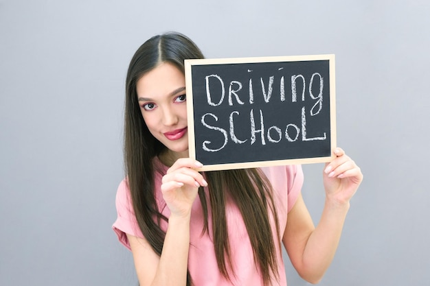 Auto-école idée et concept étudiant conducteur a réussi l'examen permis de conduire portrait d'une belle jeune femme heureuse sur une plaque de fond gris isolé avec l'inscription Auto-école