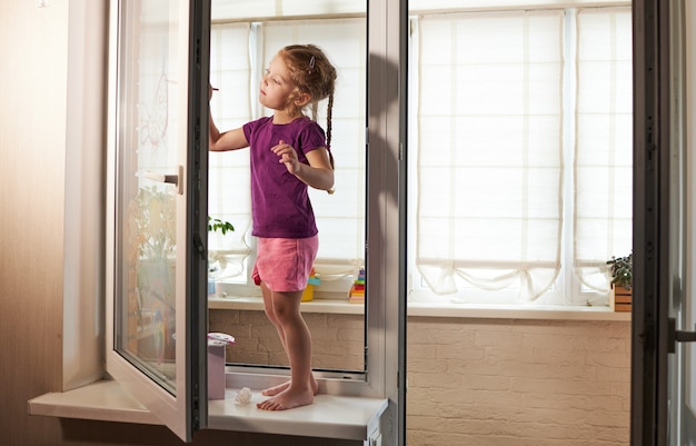 Auto-isolement à la maison. Fille enfant en quarantaine peint un arc-en-ciel sur une fenêtre en verre. Art-thérapie et apprentissage à distance