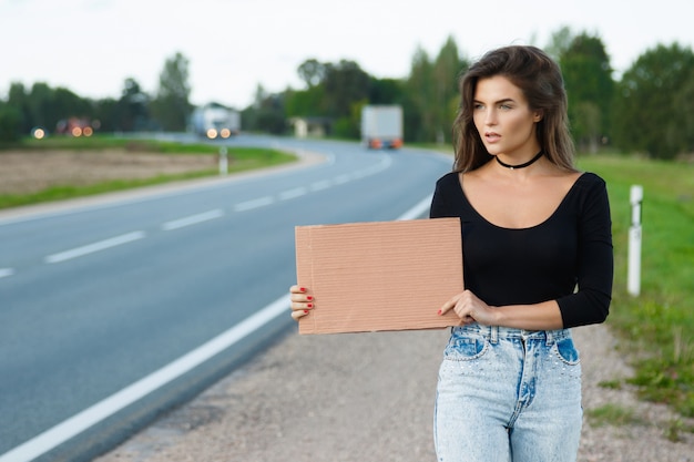 Auto-stoppeur sur la route tient une pancarte en carton vierge