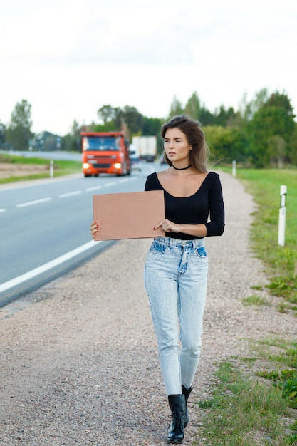 Auto-stoppeur sur la route tient une pancarte en carton vierge