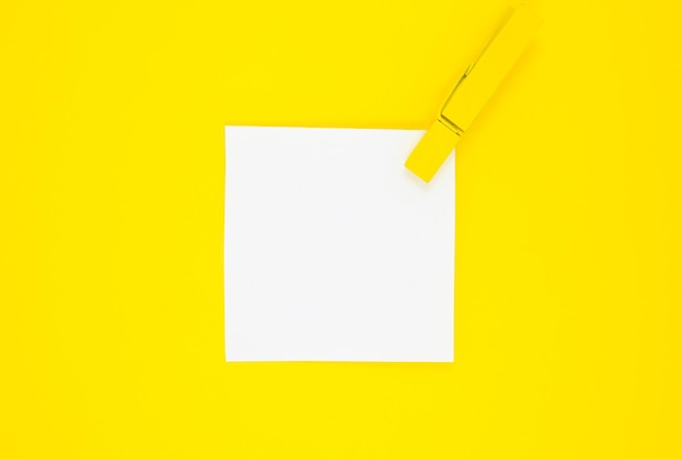 Autocollant blanc vierge de liste de tâches avec une pince à linge en bois jaune. Gros plan du papier de rappel sur le fond jaune. Espace de copie. Minimalisme, photo originale et créative.
